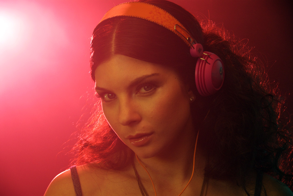 A woman wearing pink headphones bathed in saturated red light in a music video still
