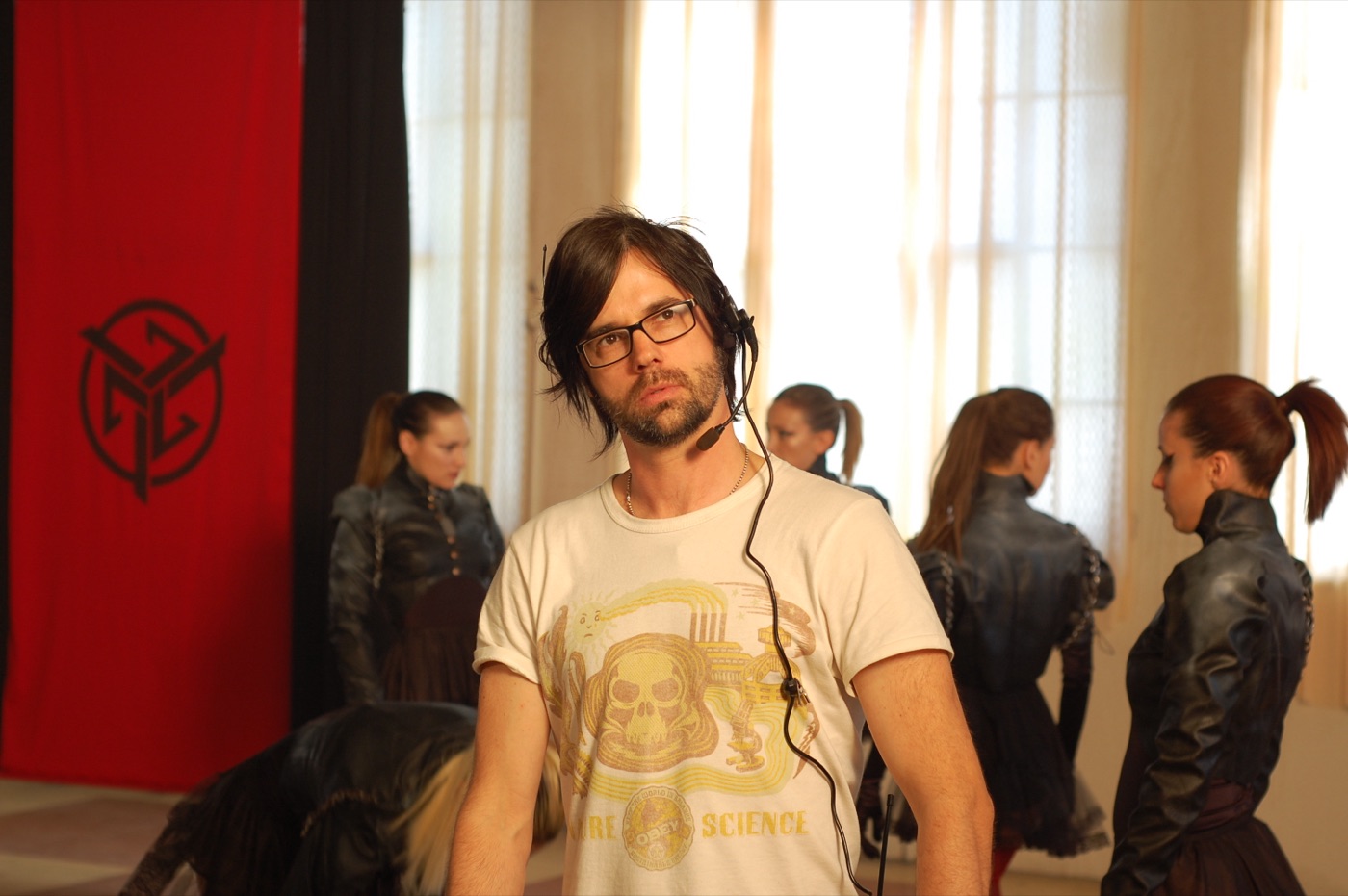 A director wearing a headset on set, surrounded by dancers in black leather costumes