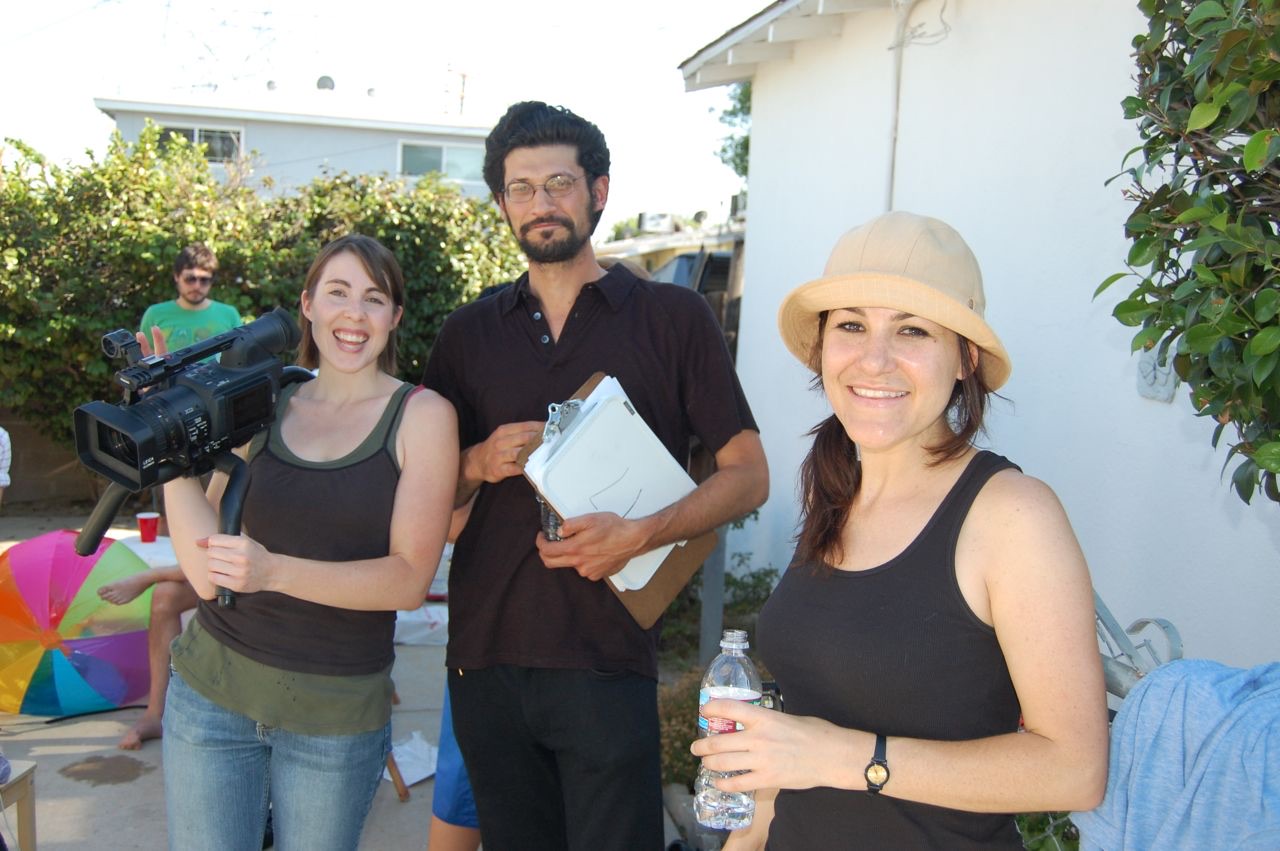 Three smiling crew members with a camera and clipboard on a sunny backyard shoot