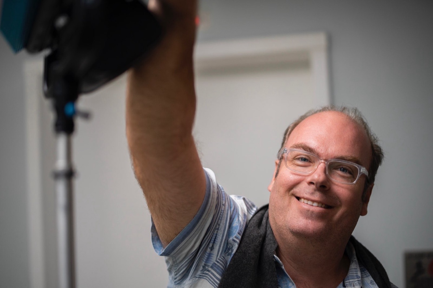 A crew member smiles while reaching up to adjust a light on a stand