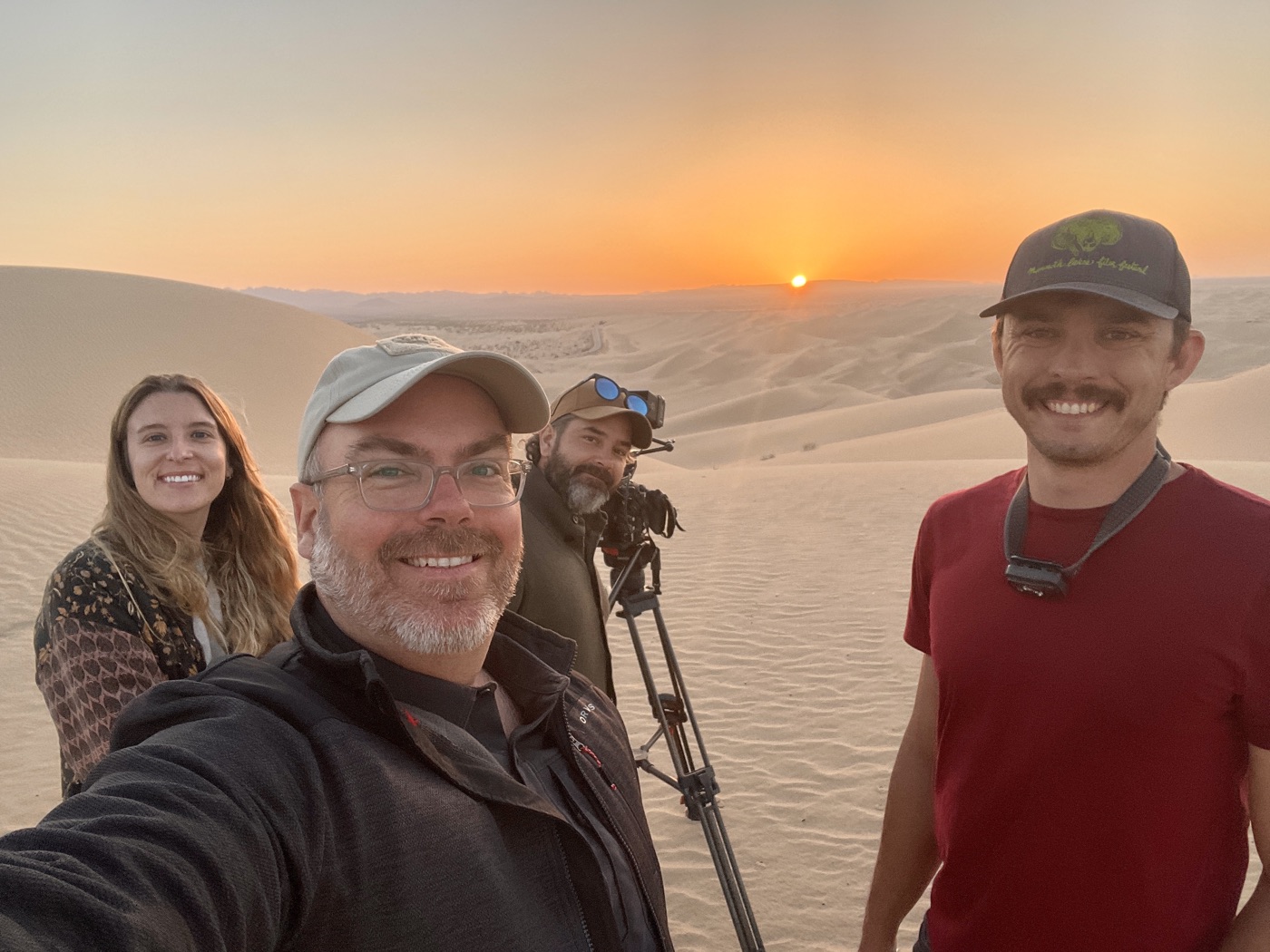 Four crew members take a selfie beside the camera at sunset in the desert dunes